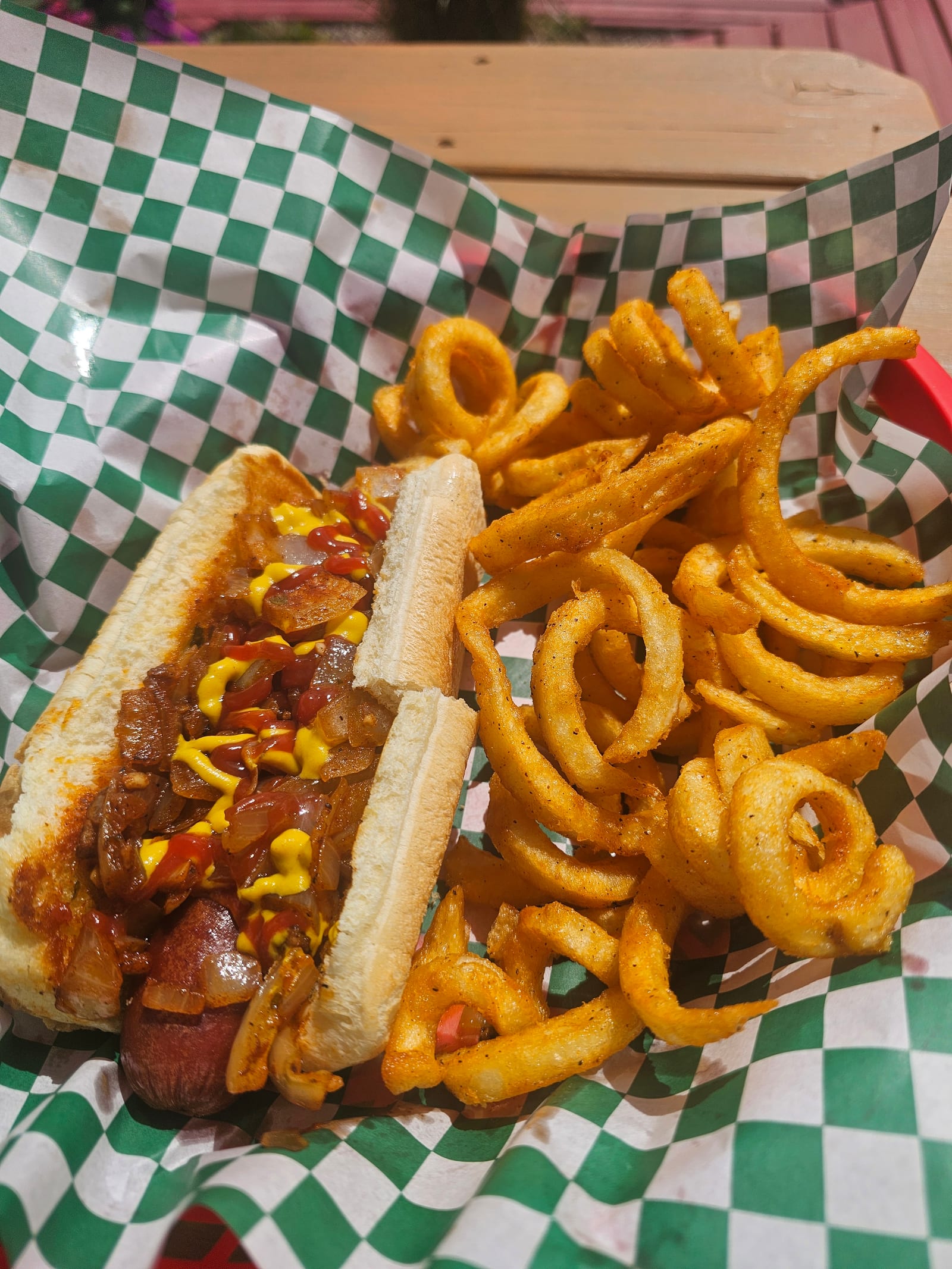 A loaded all-beef hot dog with curly onion rings in a checker-lined basket