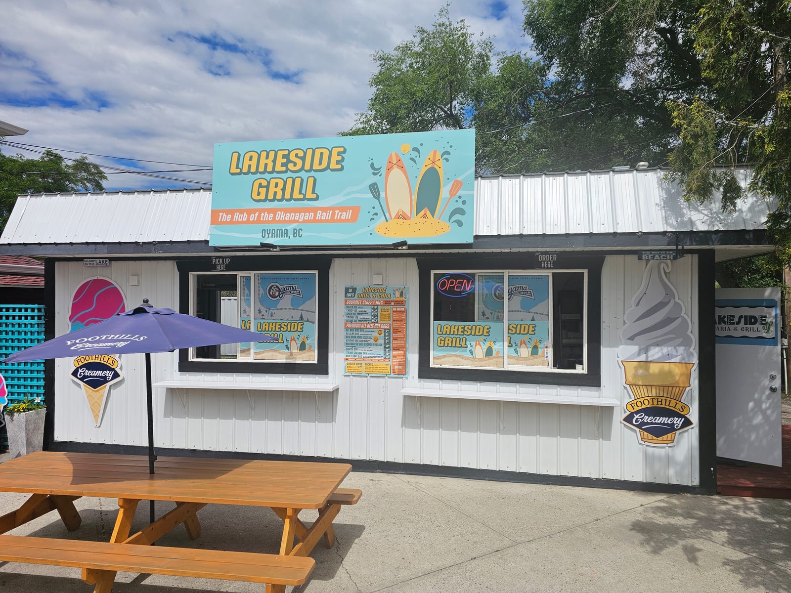 The Lu Lou's grill stand on the beach in Oyama, BC, with the orange and teal sign visible above the wooden deck
