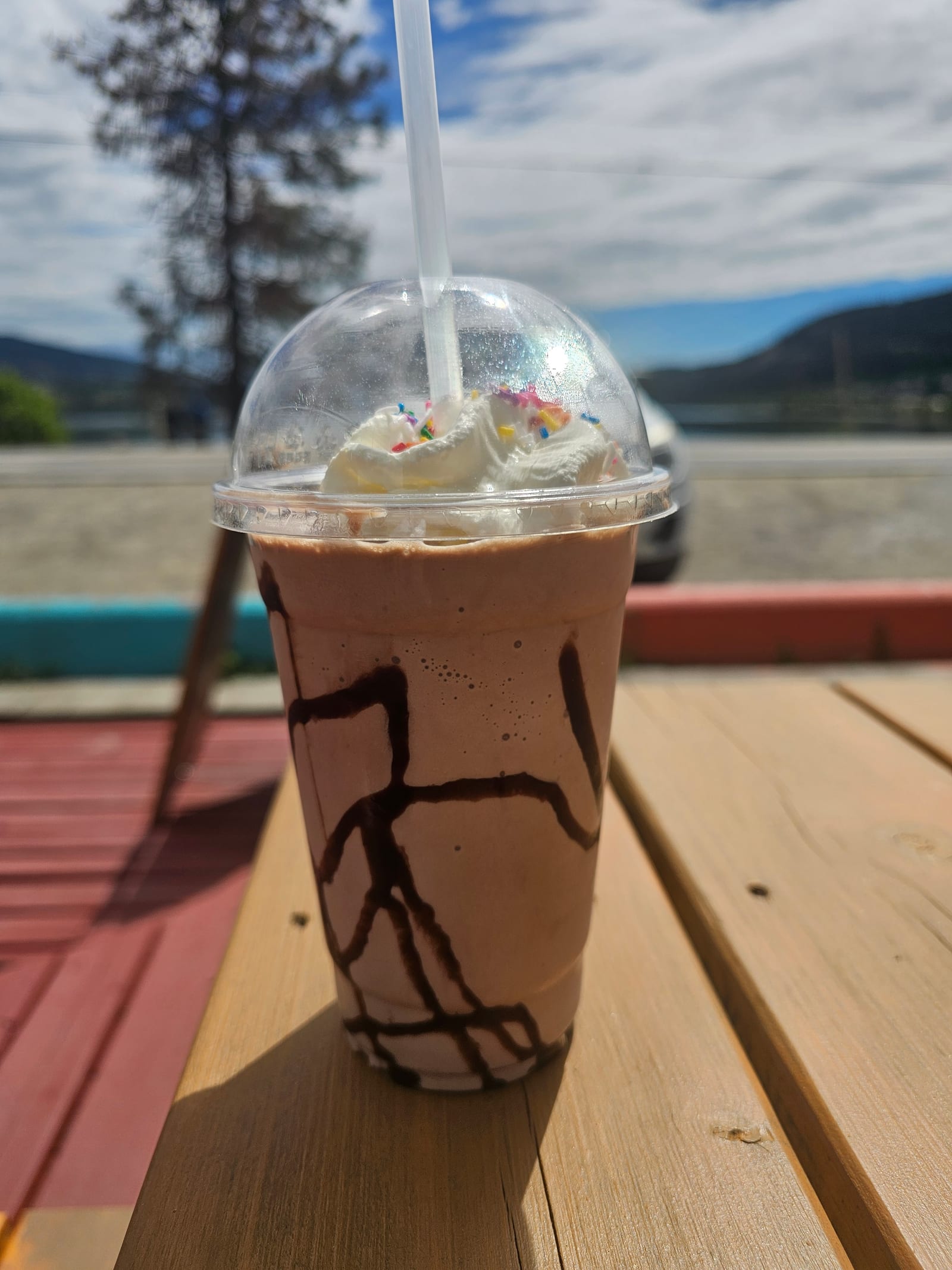 A chocolate milkshake with whipped cream on a picnic table facing Wood Lake